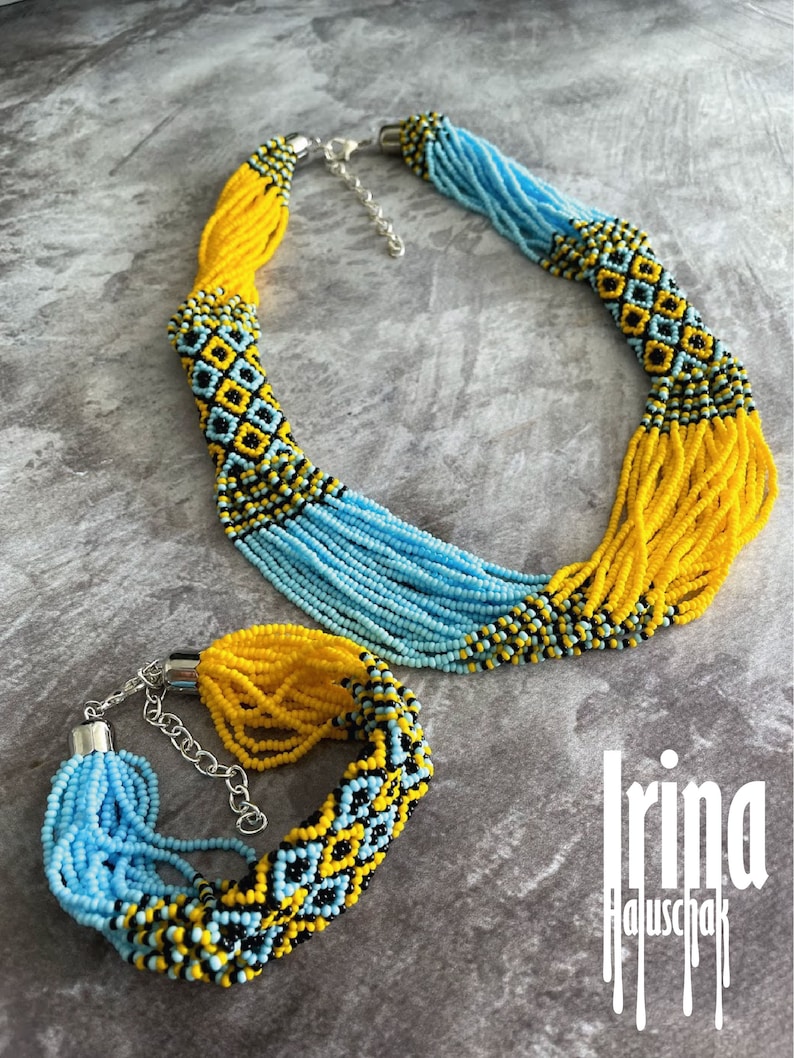 May include: A set of beaded jewelry featuring a necklace and bracelet. The necklace and bracelet are made of blue, yellow, and black beads. The beads are arranged in a geometric pattern. The necklace has a silver clasp. The bracelet has a silver clasp and a chain.