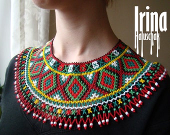 May include: A colorful beaded necklace with a geometric pattern in red, green, white, black, and yellow. The necklace has a fringe of beads around the bottom.