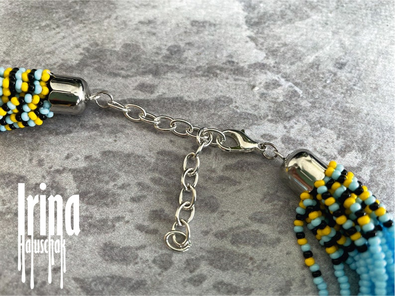 May include: A beaded necklace with a silver clasp. The beads are black, yellow, and light blue.
