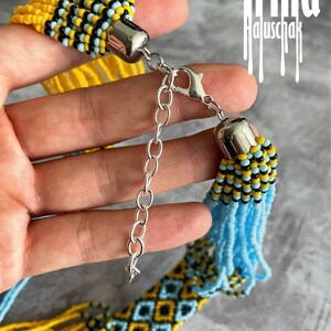 May include: A multi-strand beaded necklace with a geometric pattern in yellow, blue, and black. The necklace has a silver clasp and is made of small beads.