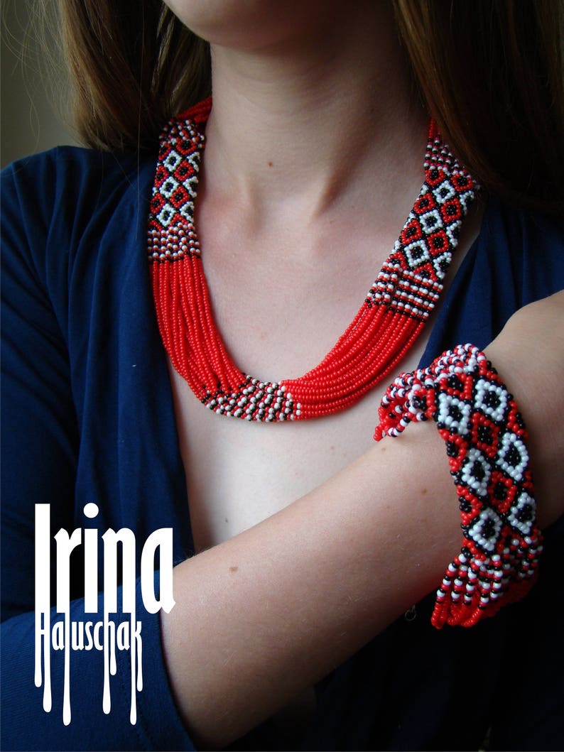 May include: A red and white beaded necklace and bracelet set with geometric patterns. The necklace is multi-strand and the bracelet is a single strand. The set is made of small, round beads.