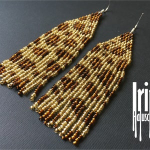 May include: Long, beaded earrings with a geometric pattern in gold and brown. The earrings are made of small, round beads and hang down to the chest.