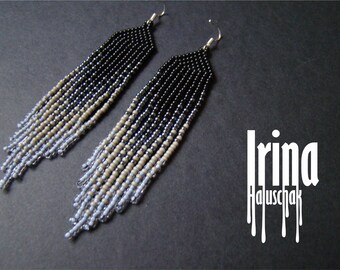 May include: A pair of long, beaded earrings with a gradient of black, beige, and light blue beads. The earrings are handmade and have a simple, elegant design.
