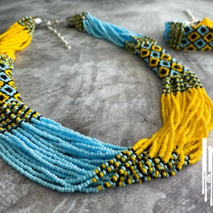 May include: A beaded necklace and bracelet set in blue, yellow, and black. The necklace is long and has a geometric pattern. The bracelet is shorter and has a similar pattern.