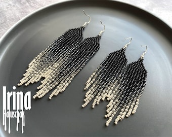 May include: A pair of long, black and white beaded earrings with a gradient effect. The earrings are made with small, round beads and hang from silver hooks.