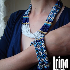 May include: A blue, white, and gold beaded necklace and bracelet set. The necklace is multi-layered and the bracelet has a fringe. The set is made with small, round beads.