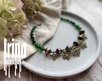 May include: A green and black beaded necklace with gold-toned cross charms. The necklace is on a gray surface.
