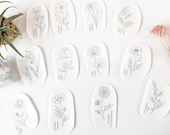 May include: Twelve white oval-shaped cards with black line drawings of flowers and their corresponding month and name. The cards are arranged in three rows of four cards each.