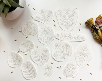 May include: A set of 12 embroidery patterns featuring various floral designs. The patterns are printed on white fabric and are ready to be stitched.