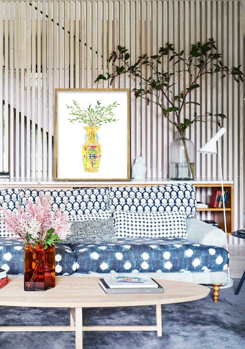 May include: A watercolor painting of a yellow and green vase with a bouquet of green leaves. The painting is framed in a gold frame and is hanging on a wall with wood paneling.