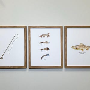 May include: Three framed prints with a fishing theme. The left print shows a fishing rod and line. The center print shows five different fishing flies. The right print shows a brown trout with the text "Brown Trout" below it.