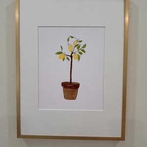 May include: A framed watercolor painting of a potted lemon tree with green leaves and yellow lemons. The frame is gold.