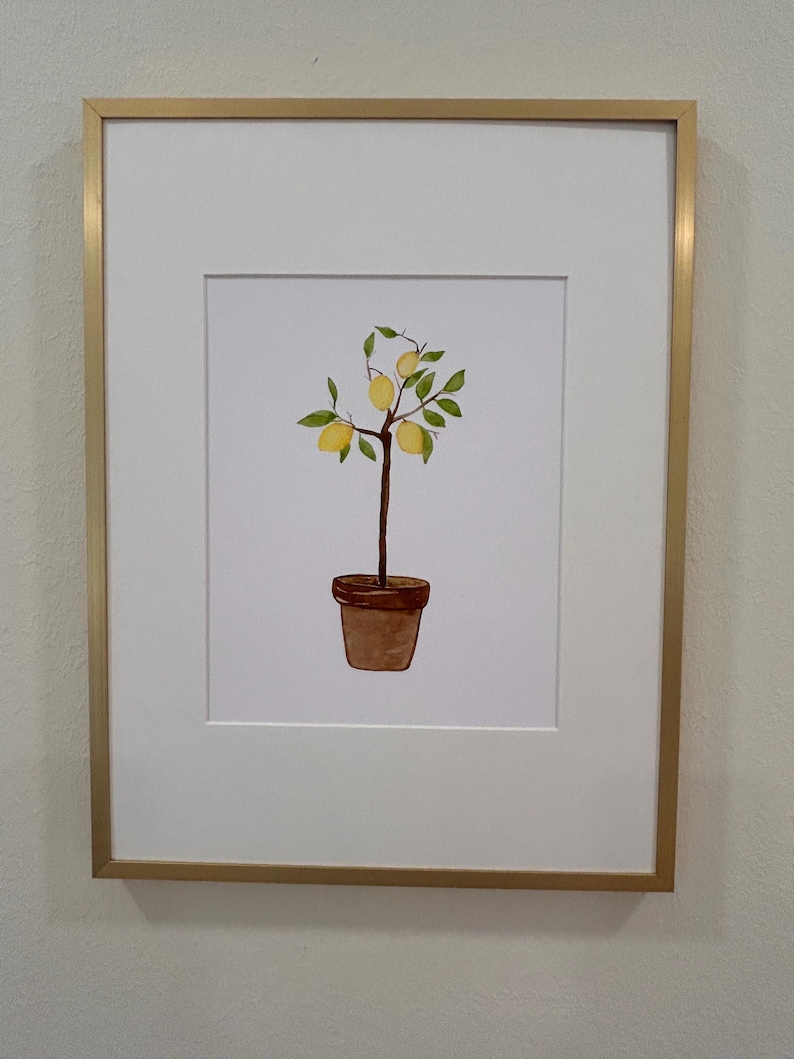 May include: A framed watercolor painting of a potted lemon tree with green leaves and yellow lemons. The frame is gold.