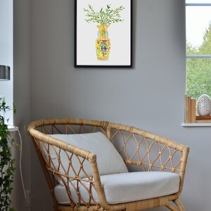 May include: A framed watercolor painting of a yellow vase with green leaves and a blue and red pattern. The vase is sitting on a white background.
