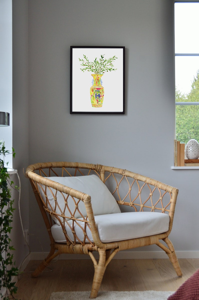 May include: A framed watercolor painting of a yellow vase with green leaves and a blue and red pattern. The vase is sitting on a white background.