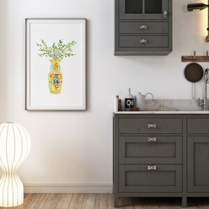 May include: A watercolor painting of a yellow and green vase with a floral design. The vase is filled with green leaves and is framed in a white frame.