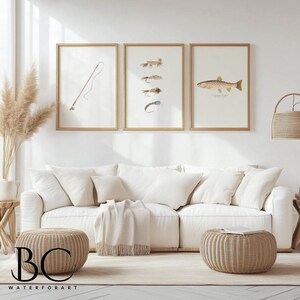 May include: Three framed prints on a white wall above a white couch with two beige ottomans. The prints are of fishing flies, a fishing rod, and a trout. The text on the print reads "Cutthroat Trout".