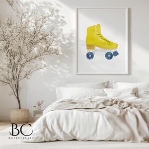 May include: A framed watercolor print of a yellow roller skate with blue wheels. The artwork is displayed on a white wall above a bed with white bedding. The room is decorated with a potted tree and a neutral color palette.