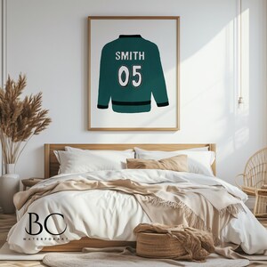 Puede incluir: Una chaqueta verde azulada con el nombre "SMITH" y el n&uacute;mero "05" en blanco en la parte posterior. La chaqueta est&aacute; colgada en una pared blanca en un dormitorio.