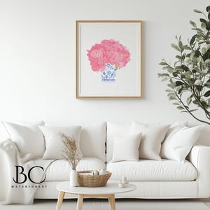 Puede incluir: Una impresi&oacute;n art&iacute;stica enmarcada con un ramo de flores rosas en un jarr&oacute;n azul y blanco. La obra de arte se exhibe en una pared blanca sobre un sof&aacute; blanco. La impresi&oacute;n tiene un marco dorado.