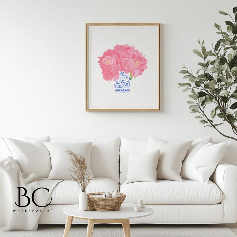 Puede incluir: Una impresi&oacute;n art&iacute;stica enmarcada con un ramo de flores rosas en un jarr&oacute;n azul y blanco. La obra de arte se exhibe en una pared blanca sobre un sof&aacute; blanco. La impresi&oacute;n tiene un marco dorado.