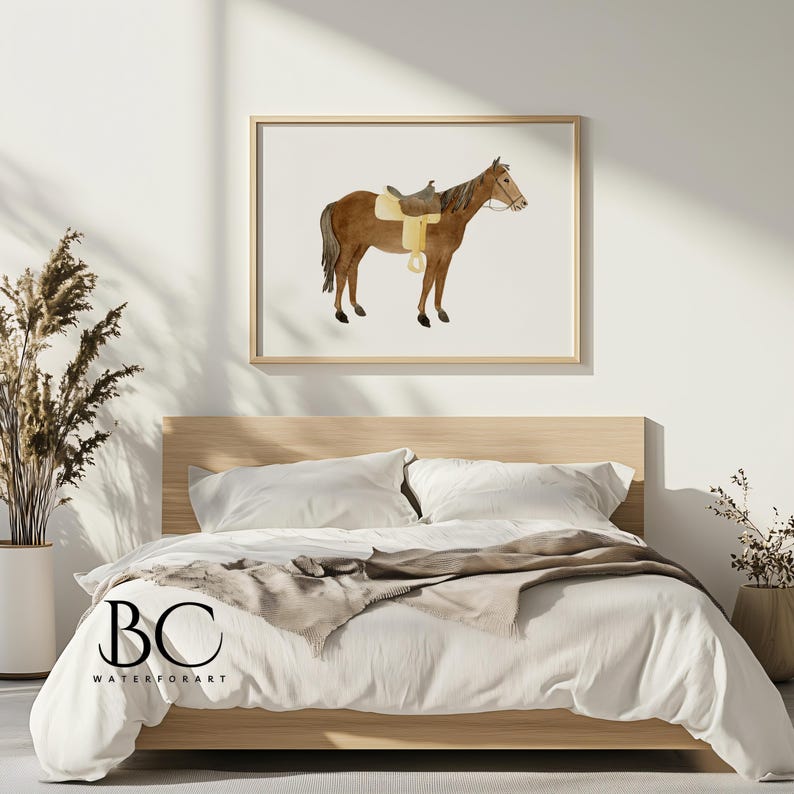 May include: A watercolor painting of a brown horse with a saddle and bridle, framed in a light wood frame and hanging on a white wall above a bed with white bedding and a brown throw blanket.