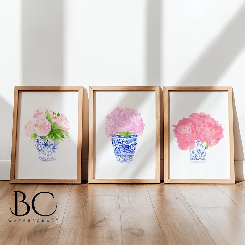Puede incluir: Tres impresiones en acuarela enmarcadas con flores rosas en jarrones con dise&ntilde;os azules y blancos. La obra de arte est&aacute; sobre un fondo blanco y enmarcada en madera clara. El texto "BC WATERFORART" est&aacute; en la esquina inferior izquierda.