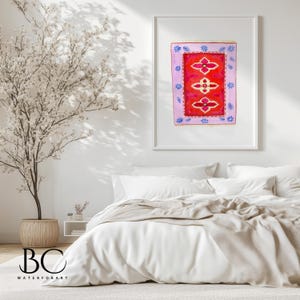 May include: A framed watercolor painting of a red rug with a floral pattern. The rug is surrounded by a pink border with blue and white accents. The painting is hanging on a white wall above a white bed with a beige blanket.