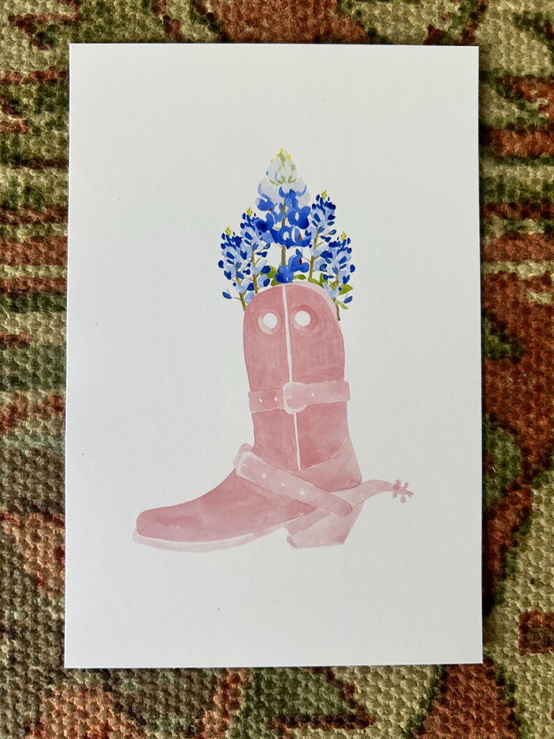 Puede incluir: Una bota vaquera rosa con espuela, decorada con flores de campanilla azul y blanca de Texas.