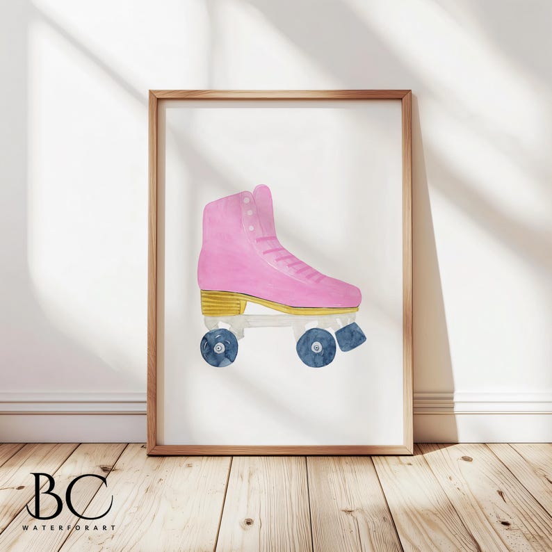 May include: A framed watercolor print of a pink roller skate with gold accents and blue wheels. The artwork is displayed on a white background and framed in a light brown wooden frame. The print is displayed on a wooden floor.