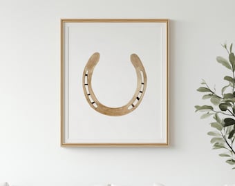 Puede incluir: Una lámina de arte enmarcada que presenta una ilustración en acuarela centrada de una herradura de color tostado con agujeros para clavos en marrón oscuro. La obra está en un marco de madera clara sobre una pared de tono neutro.