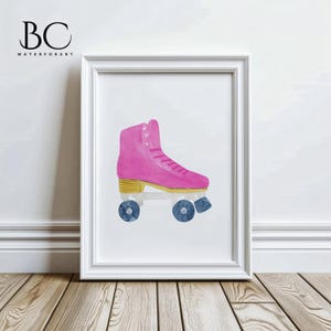 May include: A framed watercolor print of a pink roller skate. The skate has blue wheels, gold accents, and pink laces. The artwork is displayed in a white frame against a white wall and wooden floor.