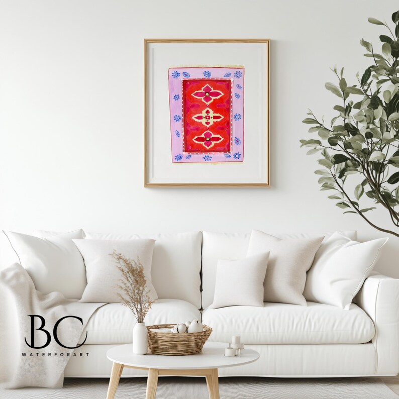 May include: A framed watercolor painting of a red and pink patterned rug with blue and white accents. The rug is surrounded by a light pink border with blue and white floral designs. The painting is hanging on a white wall above a white couch.