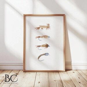 May include: A framed watercolor print of five different fly fishing lures. The lures are depicted in shades of brown and blue, with intricate details. The print is set against a white background.