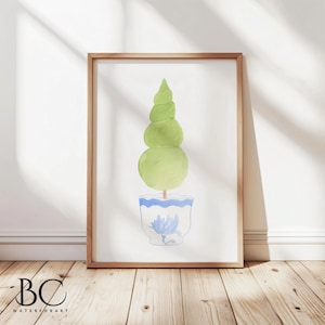 Op de afbeelding: Ingelijste aquarelprint van een groene topiary in een blauw-witte pot. De topiary heeft een spiraalvormige top en afgeronde secties. De pot heeft een bloemenpatroon. Het frame is van licht hout.