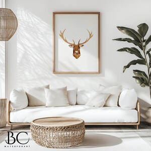 May include: A watercolor painting of a deer head with antlers in a light brown frame hanging on a white wall above a white couch with white pillows. A woven wicker coffee table sits in front of the couch.