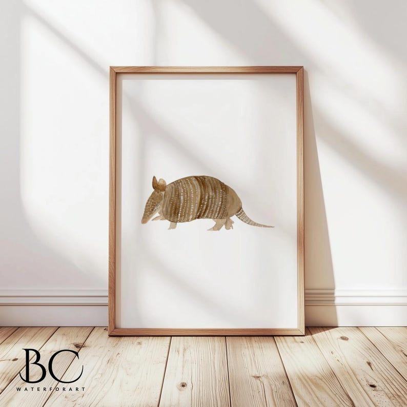May include: A watercolor painting of an armadillo on a white background. The armadillo is brown and has a textured shell. The painting is framed in a light brown wood frame.