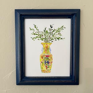 May include: A watercolor painting of a yellow vase with green leaves and small black berries. The vase has a colorful geometric pattern and is framed in a dark blue frame.