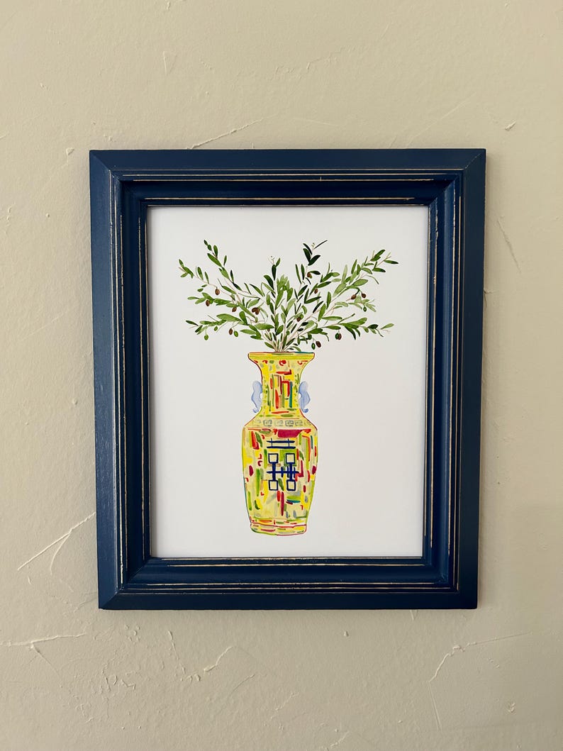 May include: A watercolor painting of a yellow vase with green leaves and small black berries. The vase has a colorful geometric pattern and is framed in a dark blue frame.