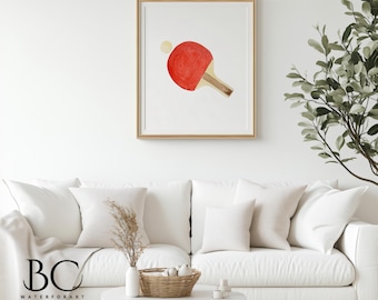 Könnte beinhalten: Ein Aquarellbild eines roten Tischtennis Schlägers mit einem weißen Ball im Hintergrund. Das Bild ist in einem hellen Holzrahmen gerahmt und hängt an einer weißen Wand.