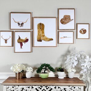May include: A set of framed watercolor prints with a western theme. The prints feature a longhorn skull, a cowboy boot, a saddle, a deer head, a cowboy hat, a rifle, and a football.