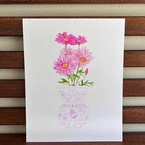 May include: A watercolor painting of a bouquet of pink daisies in a white vase with a pink floral pattern. The vase is decorated with a delicate floral design.