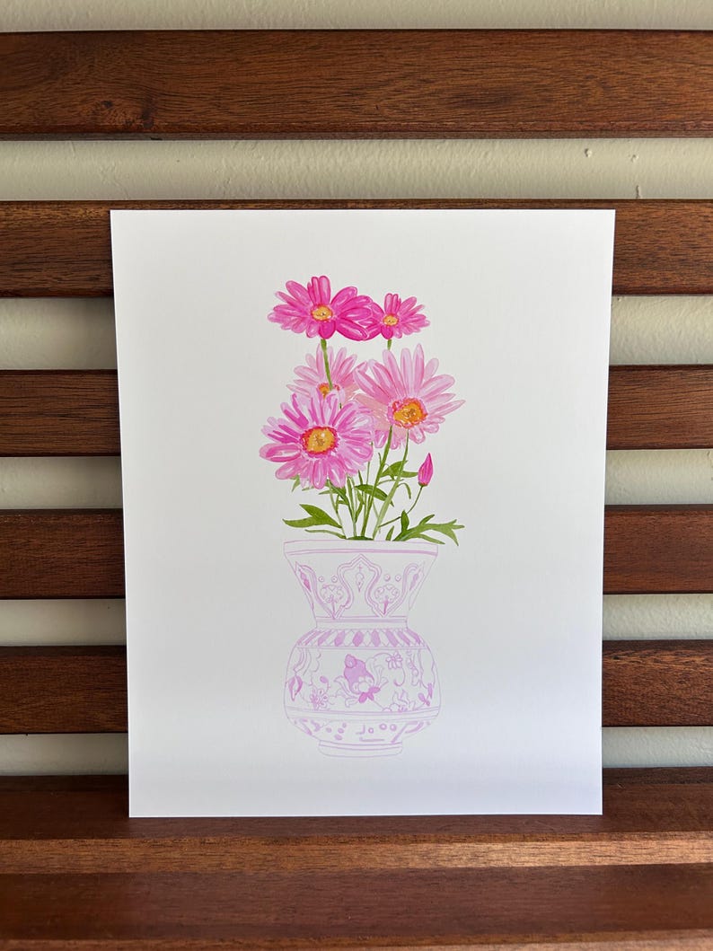 May include: A watercolor painting of a bouquet of pink daisies in a white vase with a pink floral pattern. The vase is decorated with a delicate floral design.