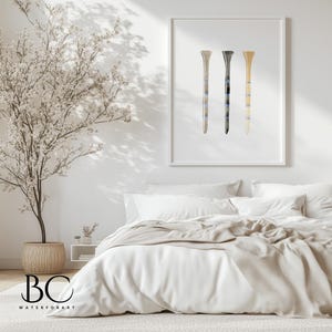 May include: A framed watercolor painting of three golf tees in different colors. The tees are arranged vertically in a row. The background is white.