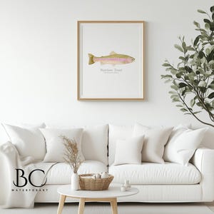 May include: A framed print of a watercolor illustration of a rainbow trout fish. The print is on a white background with the text "Rainbow Trout" and "Oncorhynchus mykiss" written below the fish.