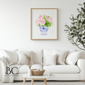 Puede incluir: Pintura a la acuarela de rosas rosas y hojas verdes en un jarr&oacute;n azul y blanco. La obra de arte est&aacute; enmarcada en un marco dorado y cuelga de una pared blanca sobre un sof&aacute; blanco. La obra de arte est&aacute; etiquetada "BC WATERFORART".