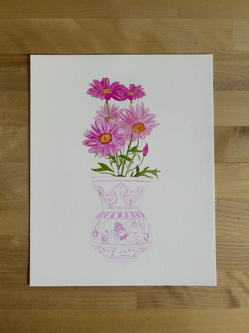 May include: A watercolor painting of a bouquet of pink daisies in a white vase with a pink floral pattern. The vase has a wide mouth and a round body.