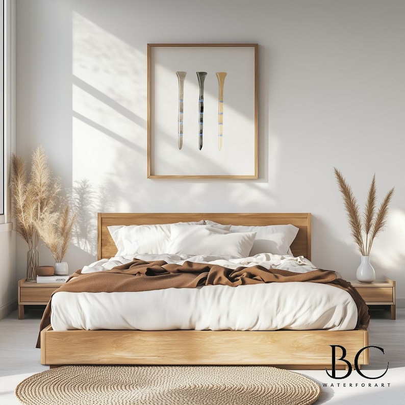 May include: A minimalist bedroom with a wooden bed frame and white bedding. A framed print of three golf tees in different colors hangs on the wall above the bed. The bed is styled with a brown throw blanket and a woven rug.
