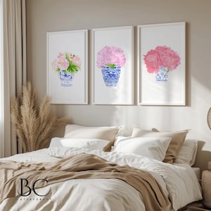 Puede incluir: Tres impresiones en acuarela enmarcadas con flores rosas en jarrones azules y blancos. Los jarrones tienen un dise&ntilde;o chino cl&aacute;sico. La obra de arte se exhibe sobre una cama con ropa de cama blanca y una manta marr&oacute;n.