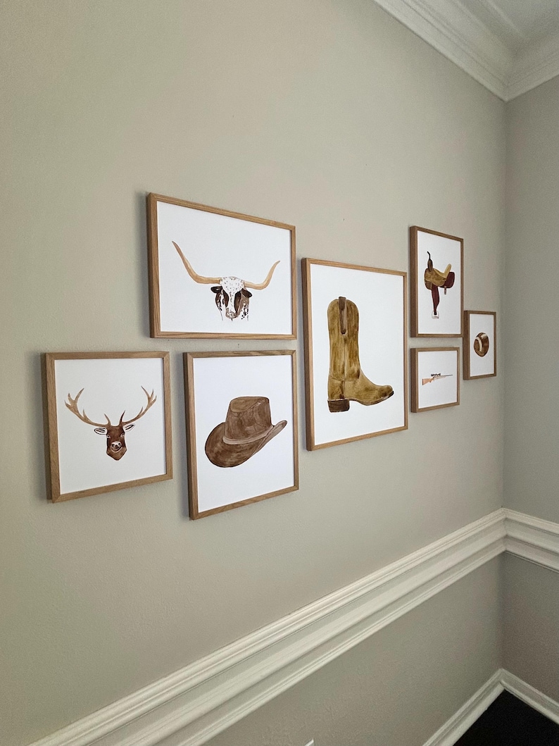 May include: A gallery wall with nine framed prints featuring various western-themed illustrations. The prints include a longhorn steer head, a cowboy boot, a cowboy hat, a deer head, a saddle, a rifle, and a lasso.
